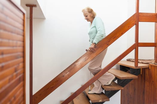 Elderly woman at home using a walking cane to get down the stairs