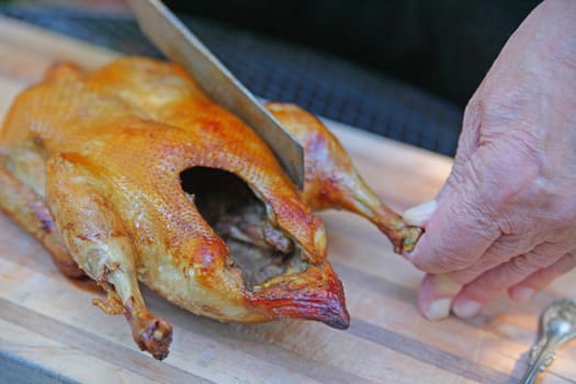 An older man carving a roast duck outdoors