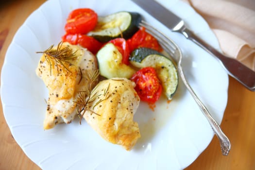White plate with chicken breast pieces, zucchini, tomatoes and rosemary