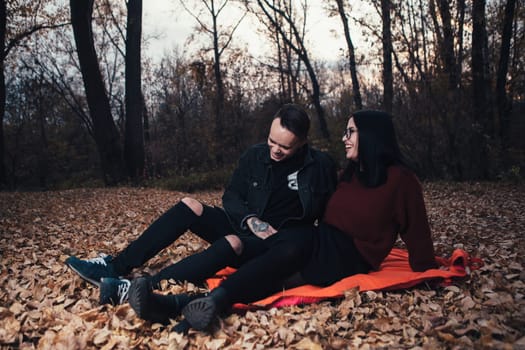 young man and young woman are sitting on a plaid in an autumn forest.