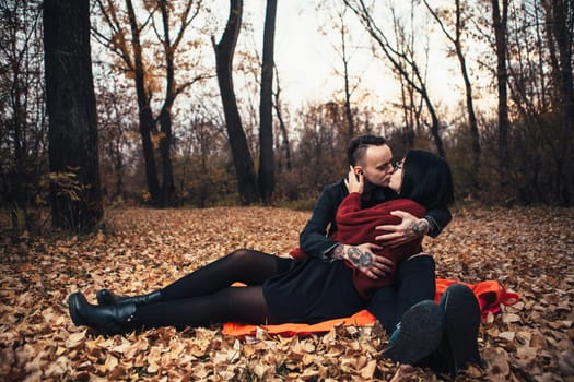 young man and young woman are sitting on a plaid in an autumn forest.