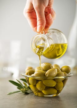 Organic olive oil. Bottle of Extra virgin oil pouring in to glass bowl with olives