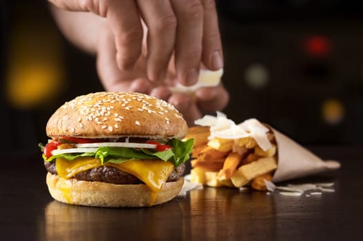 Hand that arranges beef burger with fried potatoes and cheese