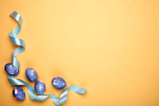 Colored easter eggs, decorative ribbon on a yellow background. Top view with copy space. Greeting card, Easter background