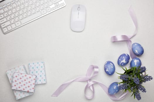 Colored easter eggs, gift box, computer keyboard and mouse on a lilac background. Top view with copy space. Greeting card, Easter background