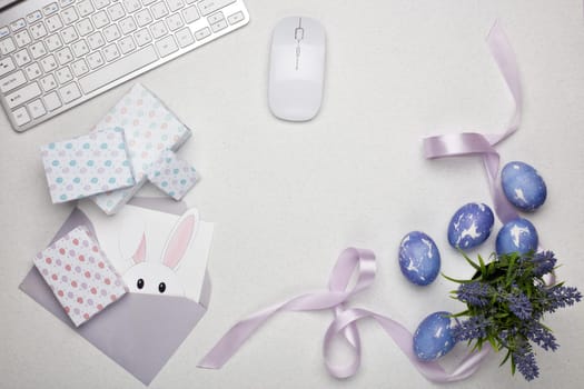 Colored easter eggs, gift box, computer keyboard and mouse, blank sheet with envelope on a lilac background. Top view with copy space. Greeting card, Easter background