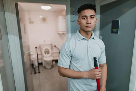 Portrait of a young, male cleaner at work. He is holding a mop.
