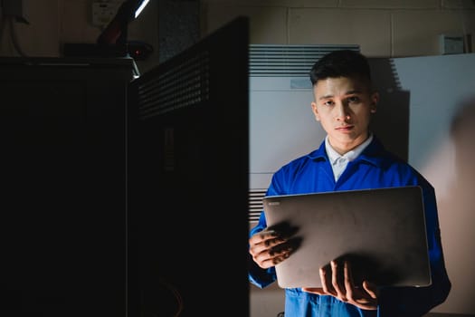 Young man is looking at the camera while in the server room with a laptop.