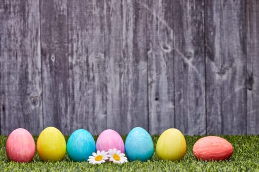 Colored easter eggs lying on a green grass on a grey wooden background with copy space. Greeting card, Easter background