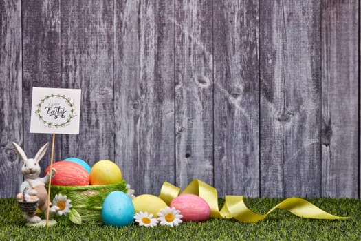 Colored easter eggs, easter rabbit and flowers lying on a green grass on a grey wooden background with copy space. Greeting card, Easter background