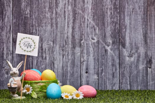 Colored easter eggs, easter rabbit and flowers lying on a green grass on a grey wooden background with copy space. Greeting card, Easter background
