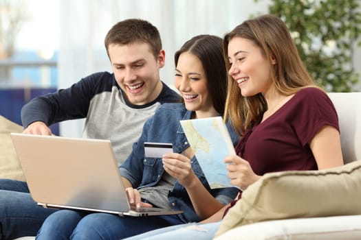 Three friends planning and buying a travel on line with a credit card and a laptop sitting on a couch in the living room at home