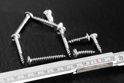 Screws and folding meter stick visualize constructional housebuilding. Symbol of self-made dream plan or craftsmanship wealth power.