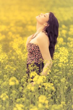 Attractive young woman enjoying the warm sunny sun in nature rapeseed field takes time feeling sustainability and contemplation.