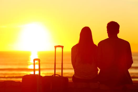 Back view backlight silhouette of a couple of travelers looking at sun on vacation travel