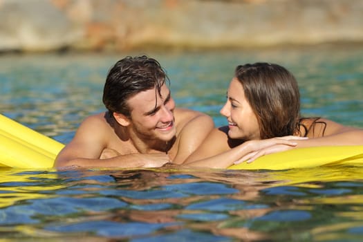 Couple flirting floating on an inflatable bed on the beach on summer vacation