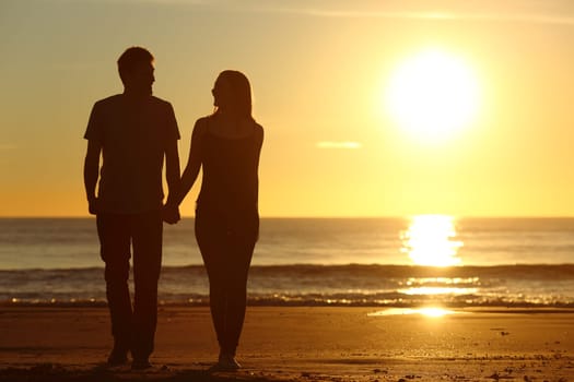 Front view of a full body of a couple silhouette walking together on the beach at sunset in summer