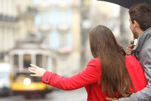 Back view of a couple waiting for public transportation and asking for a tram in the street in a rainy day