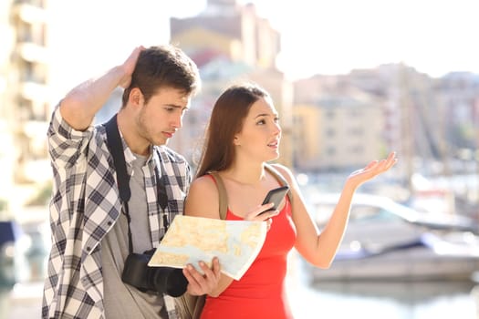 Lost couple of tourists searching location in a guide and smart phone with a port in the background