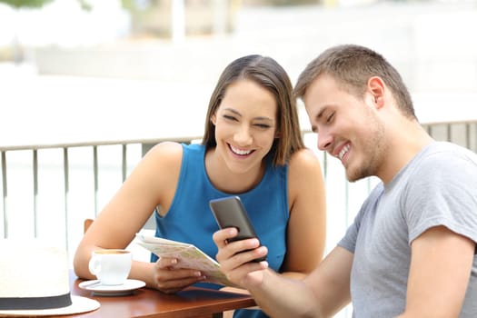 Couple of tourists searching on line locations in a smart phone and guide during travel sitting in a coffee shop