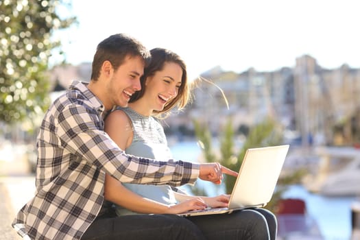 Happy couple uses a laptop sitting in a port on summer vacation