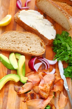Bread, smoked salmon, avocado, cream cheese, onions and lettuce on a cutting board