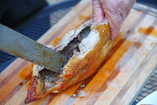 A man uses an old knife on a roast duck on a cutting board