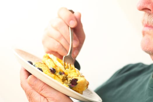 An older man holds a fork and a dish of pancakes with room for text
