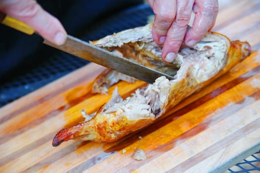 A man cuts up a roast duck on a cutting board outdoors
