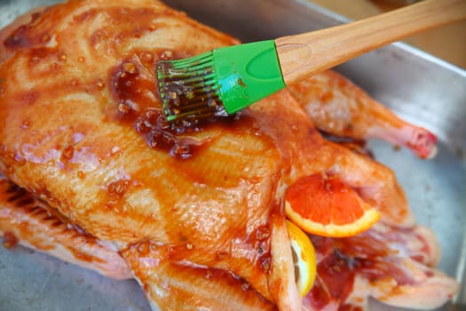Brushing a savory sauce over a duck before roasting