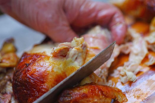 Man grasps chicken, using a kitchen knife to cut off pieces