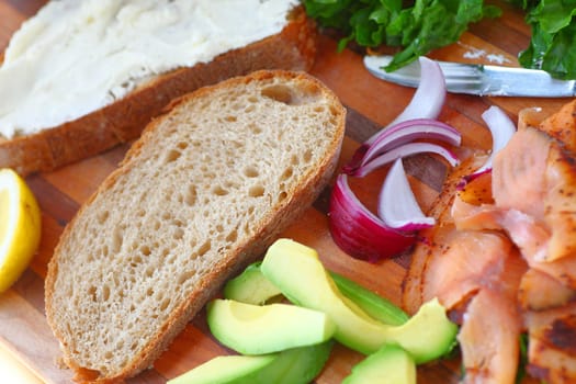 Ingredients for a homemade smoked salmon sandwich with lettuce, red onion, avocado, bread and smoked fish