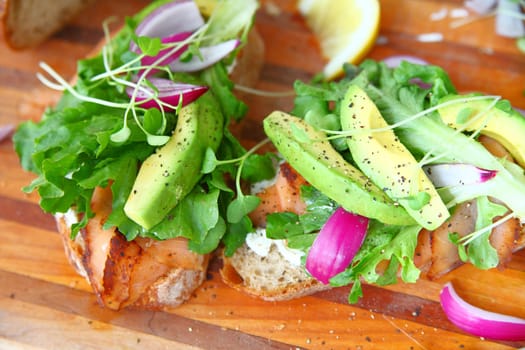 Smoked salmon sandwich preparation with avocado, onion, lettuce and sprouts