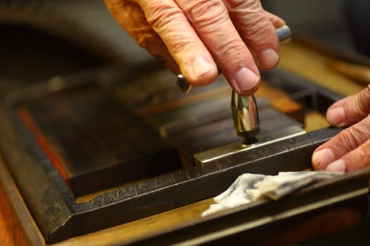 Closeup of ink-stained fingers of man using a quoin key to prepare type for letterpress printing.