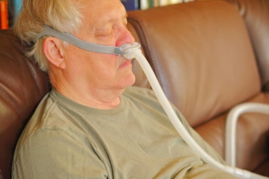 A man with sleep apnea rests on sofa, wearing a machine to help his breathing