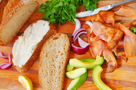 Overhead view of artisan bread slices, smoked salmon slices, avocado, red onion, lettuce and cream cheese