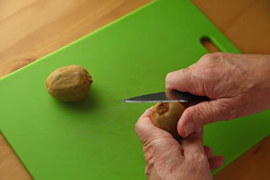 An older man peels a kiwifruit over a green cutting board