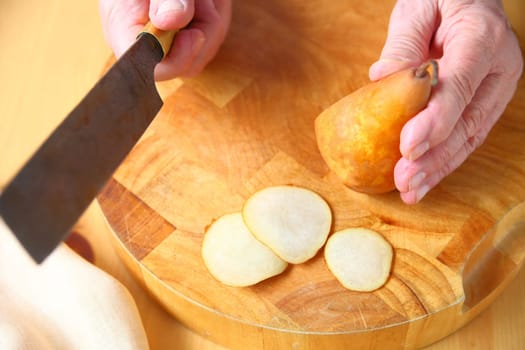 Overhead view of an older man with a ripe pear and kitchen knife on a cutting board.