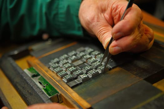 A man uses tweezers to arrange decorative metal type