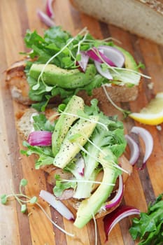 Vertical view of smoked salmon sandwiches with avocado, onions and sprouts on cutting board
