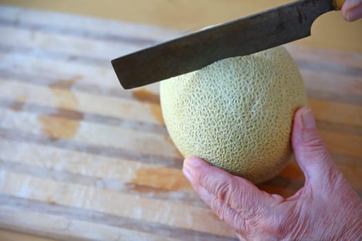 Using an old kitchen knife, a man makes a cut on a cantaloupe