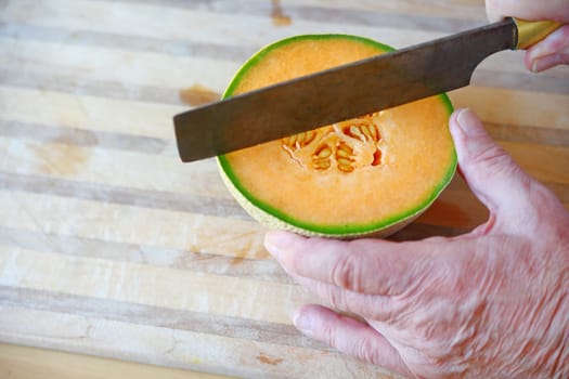 Senior cuts into fresh cantaloupe half on cutting board with room for text