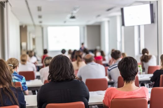 Female speaker giving presentation in lecture hall at university workshop. Audience in conference hall. Rear view of unrecognized participant in audience. Scientific conference event.