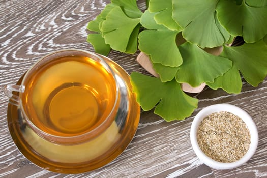 ginkgo tea in a glass cup with fresh leaves and dried herb
