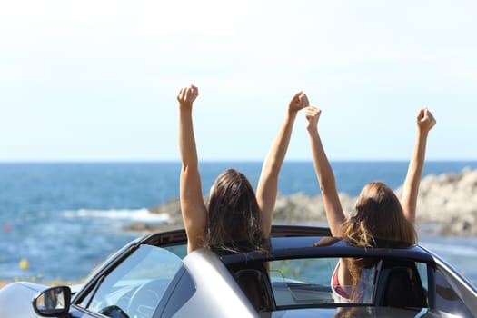 Back view of two joyful tourists watching the sea in a convertible car on summer vacation