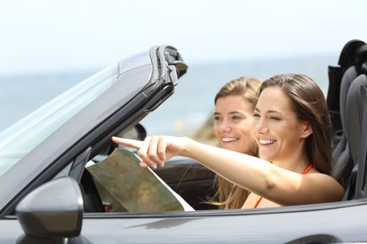 Two happy tourists in a convertible car consulting guide and pointing landmarks on summer vacations