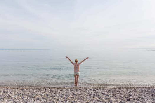 Happy Carefree Woman Enjoying Late Afternoon Walk on White Pabbled Beach in Summer.