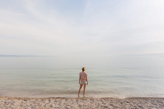 Happy Carefree Woman Enjoying Late Afternoon Walk on White Pabbled Beach in Summer.