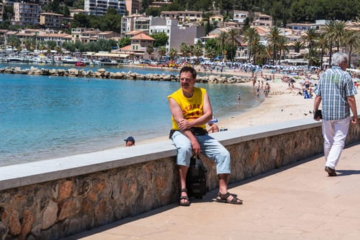 PORT DE SOLLER, SPAIN - JUNE 02, 2016:.Tourist on the wall of the beach promenade of Port de Soller in Mallorca, Spain.