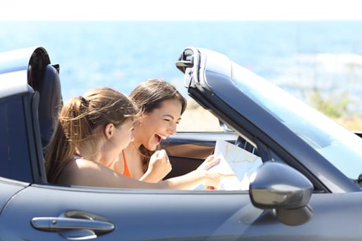 Excited tourists reading a paper map in a car on summer vacation